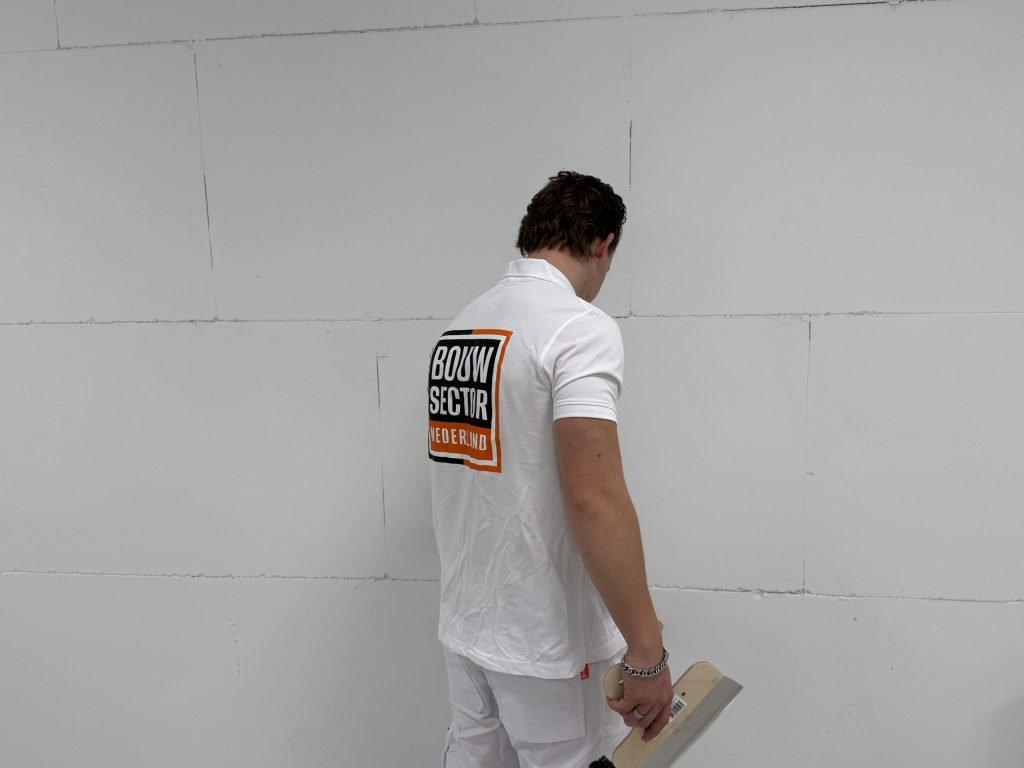 Stukadoor van Bouwsector Nederland bekijkt met een plakspaan in de hand een muur van dichtbij