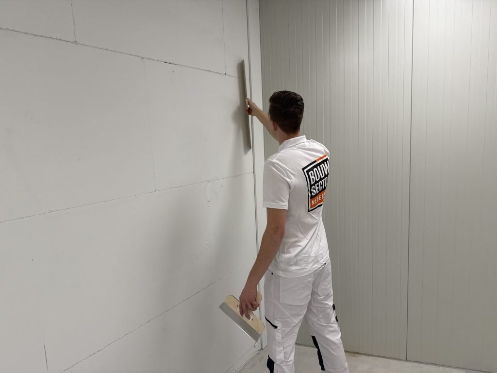 Stukadoor werkt met een lange spaan en een plakspaan aan een hoge wand van gipsblokken