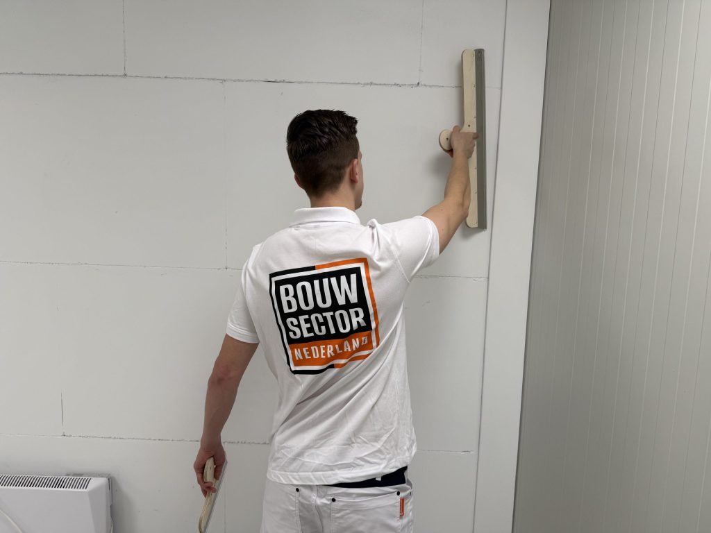 Stukadoor met het Bouwsector-logo op zijn shirt strijkt een binnenmuur glad met een lange spaan