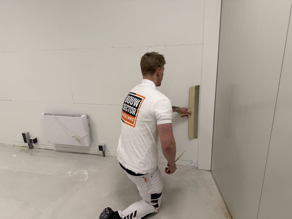 Stukadoor van Bouwsector Nederland op een knie trekt het onderste deel van een wand vlak boven de vloer