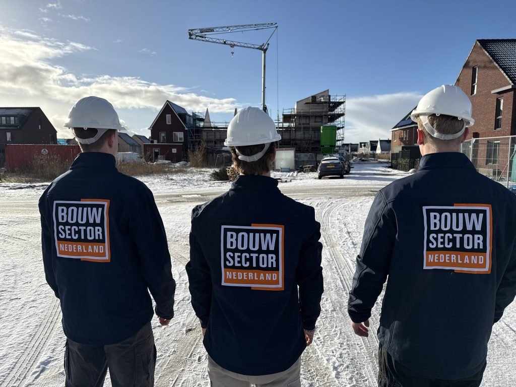 Drie medewerkers van Bouwsector Nederland met helm en werkjas kijken naar een straat met nieuwbouw